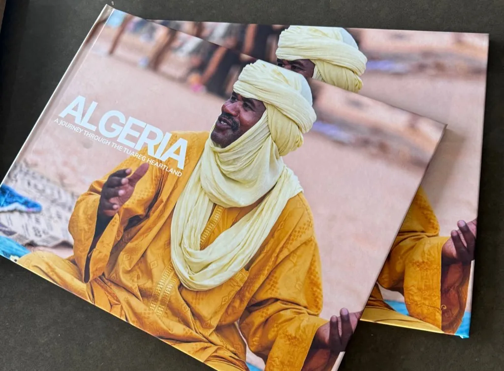 Two printed copies of the Algeria photobook, showing a Tuareg man in a yellow robe and turban.