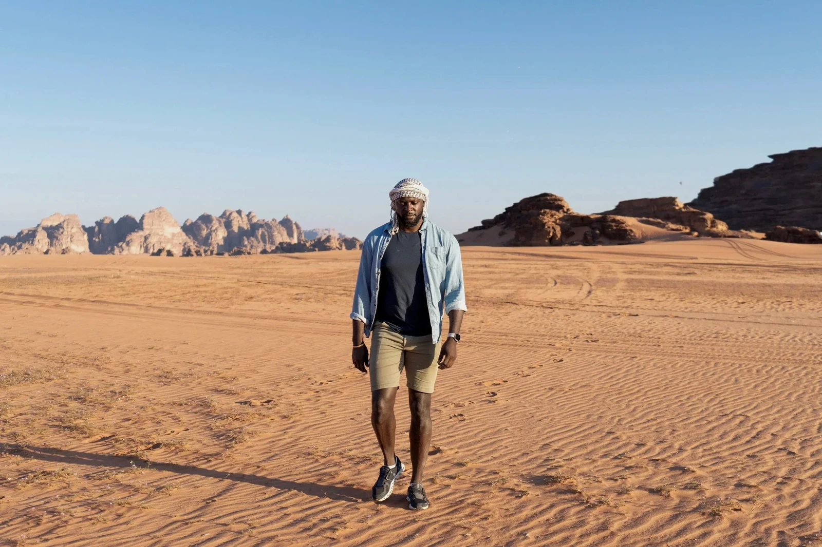 Mario Rigby walking across the desert, with rocky formations behind him.