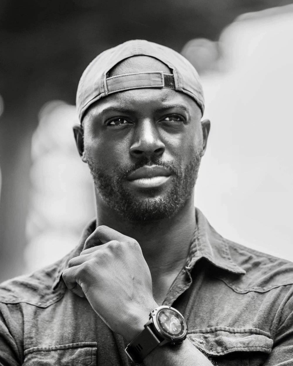 Black-and-white portrait of Mario Rigby, wearing a backwards cap with his hand resting near his chin.