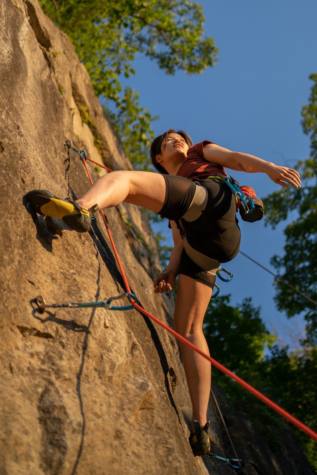 A climber pulling up a sunlit rock face