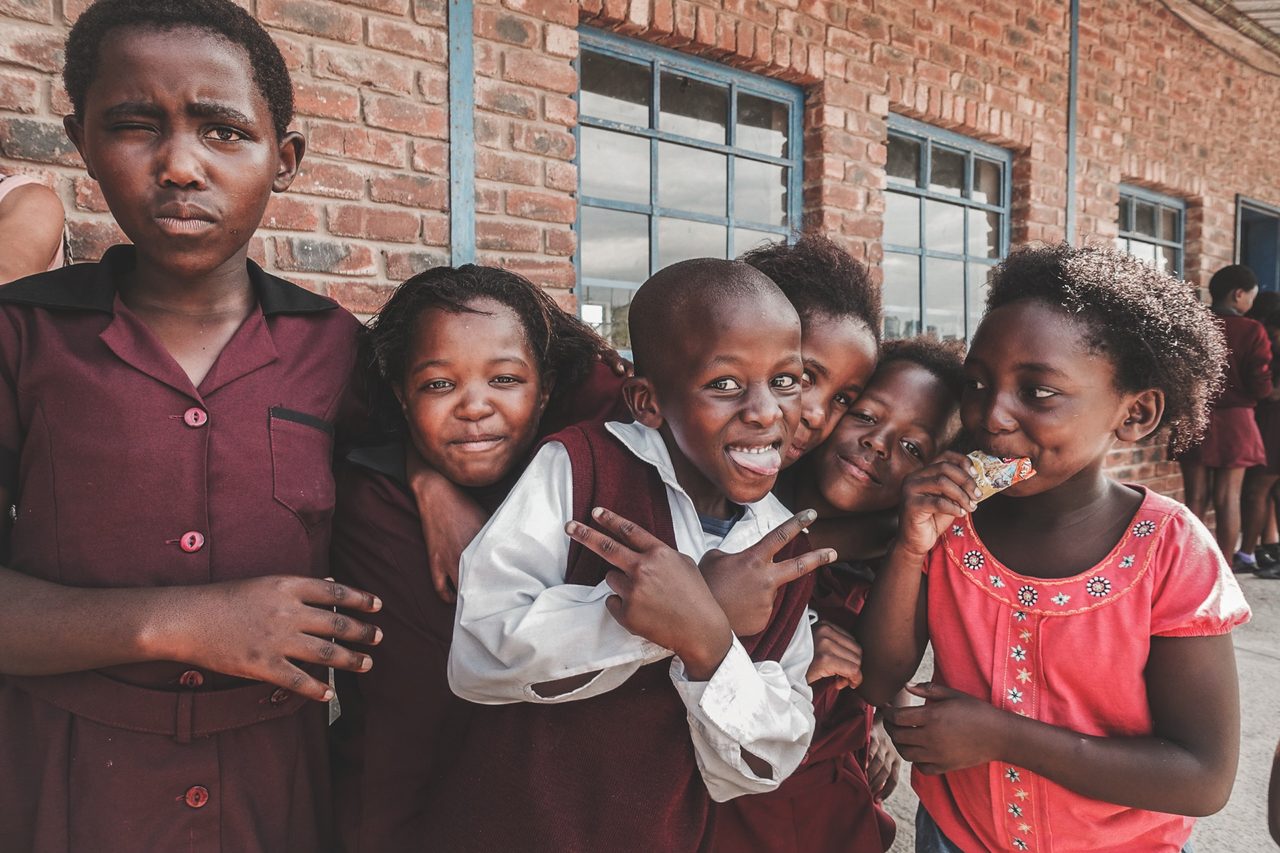 A group of schoolchildren smiling together outside a brick building