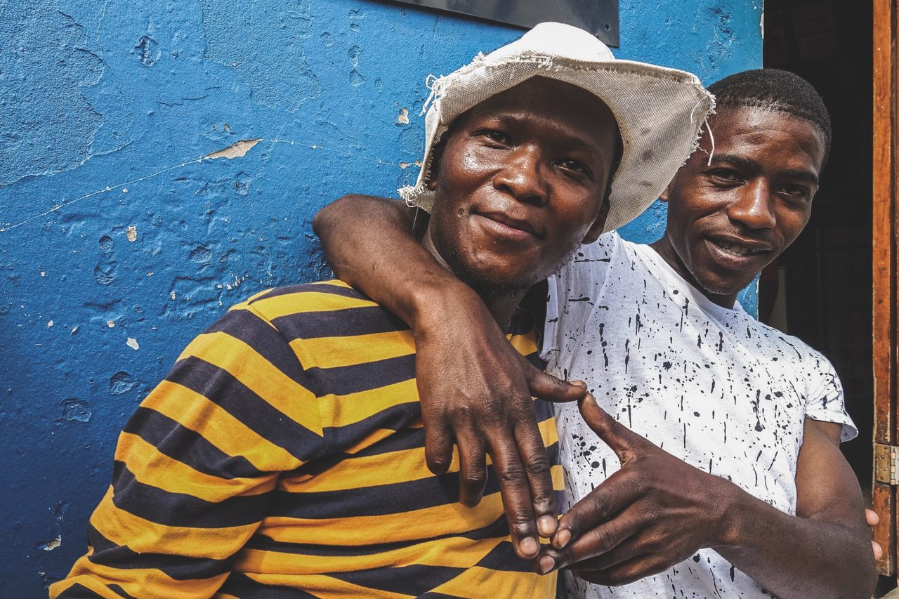 Two friends embracing and smiling in front of a blue wall